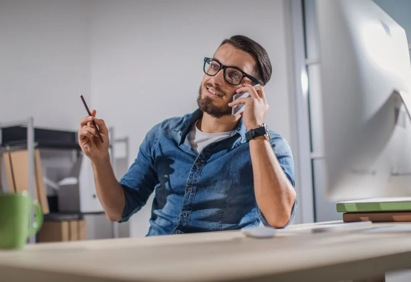 a-person-in-glasses-talking-on-the-phone-while-sitting-at-their-desk