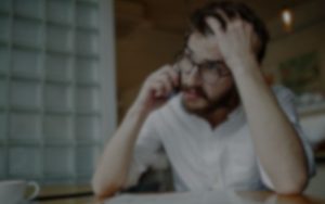 A person with glasses sits at a table and talks on the phone